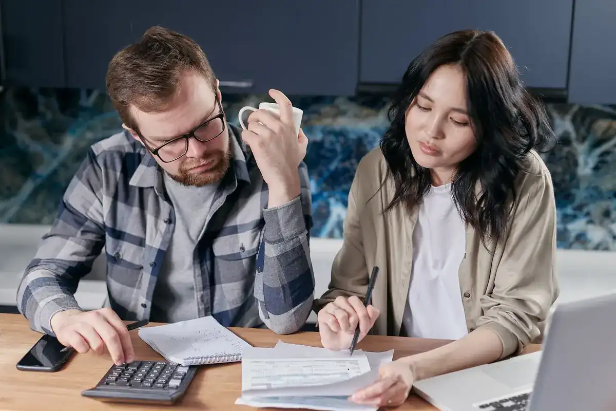 Couple working through loan paperwork with a calculator and laptop at a kitchen table