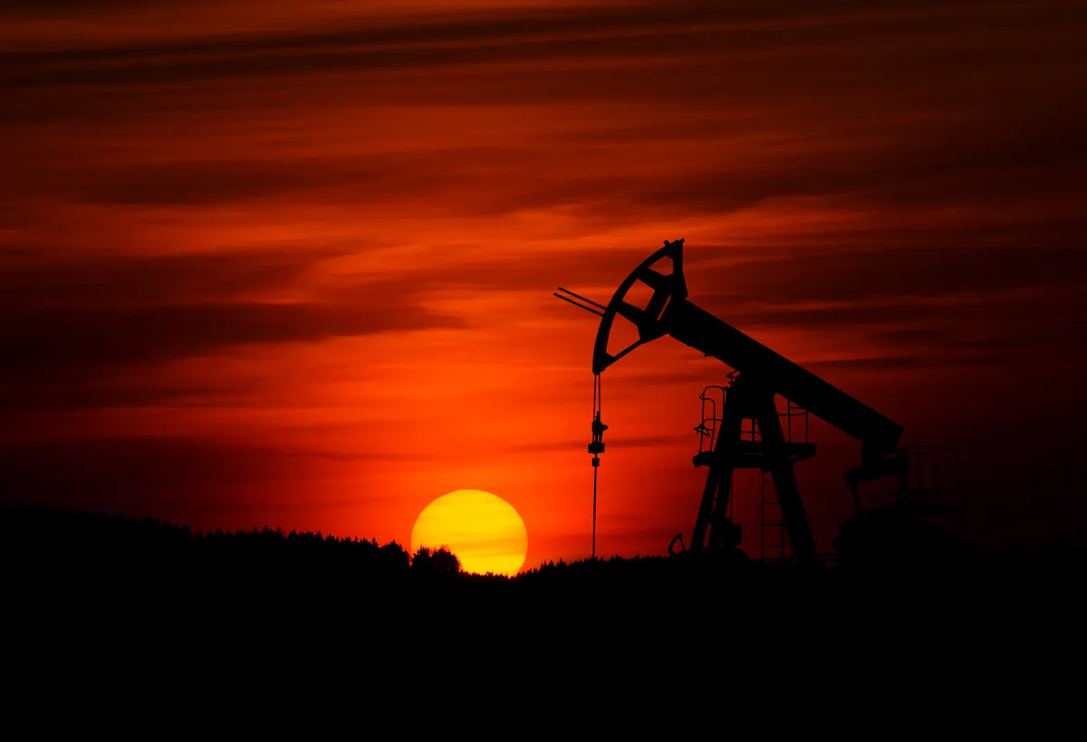 Silhouette of an oil pump jack against a red sunset sky