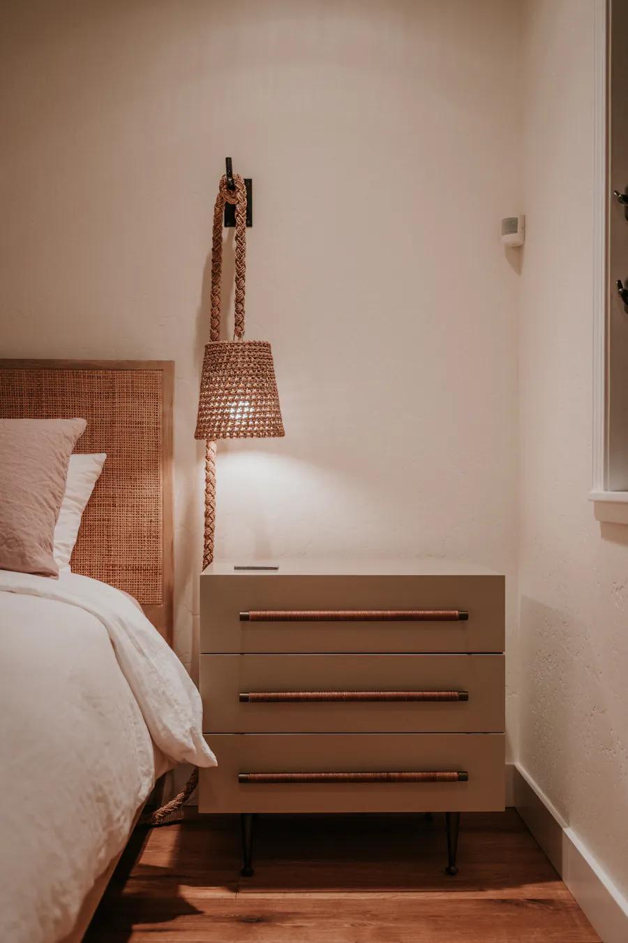 Warm, boutique-styled bedroom with rattan bedhead and woven pendant lamp