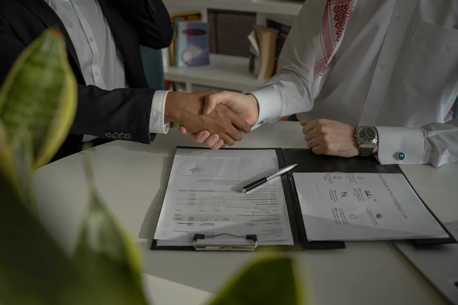 Two people shaking hands over signed documents on a desk