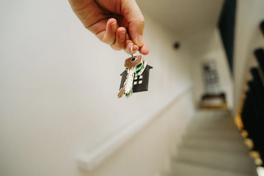 Hand holding a house-shaped keychain with keys at a front entrance